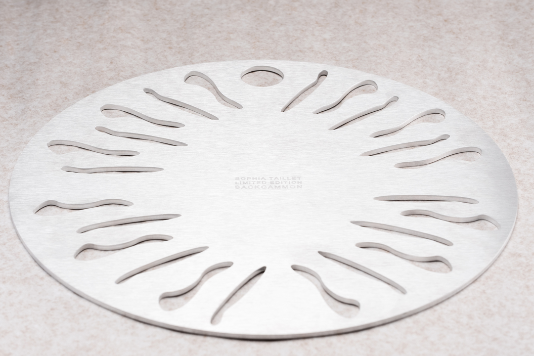 Silver metal round backgammon board with curved slots and the words 'Sophia Taillet Limited Edition' etched in the center.