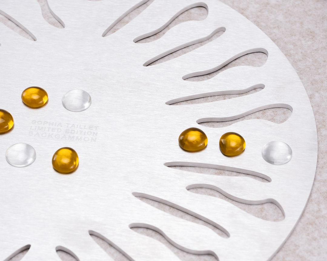 Close-up of a limited edition Sophia Taillet backgammon board with amber and translucent game pieces against a neutral background.