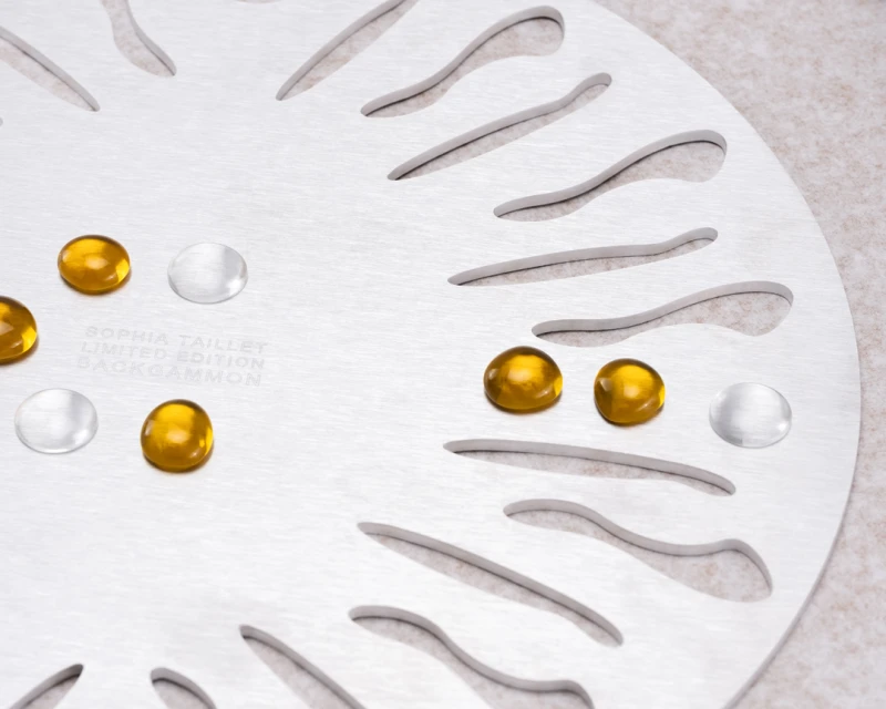 Close-up of a limited edition Sophia Taillet backgammon board with amber and translucent game pieces against a neutral background.