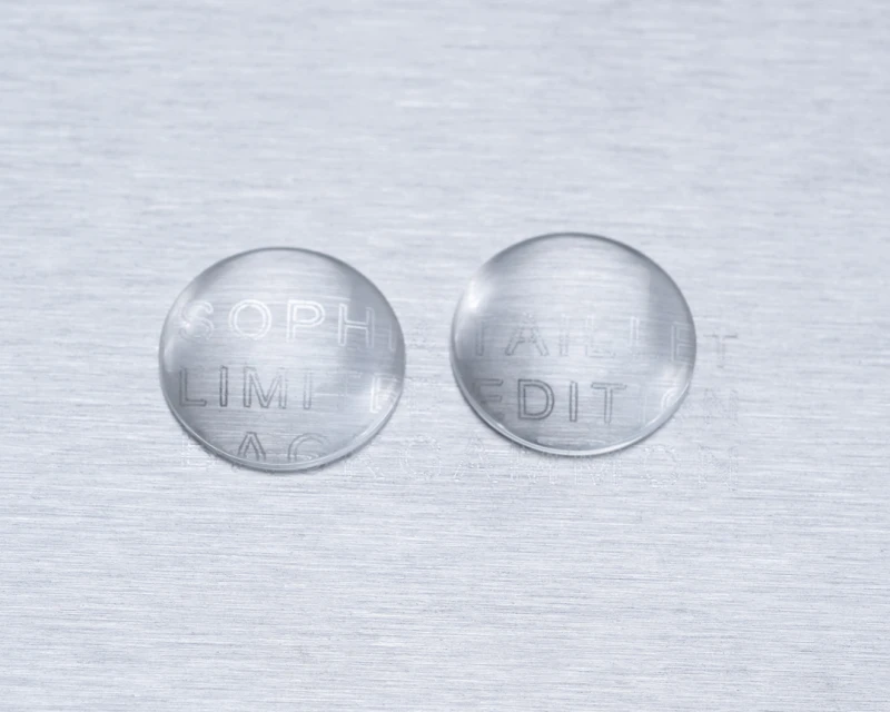 Two clear, round objects with etched text on a brushed metal surface, creating a minimalist and modern abstract composition.