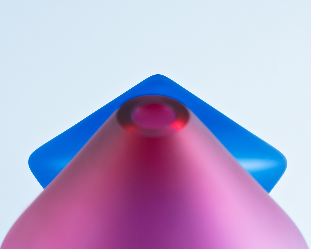 Abstract still life of a pink cone shape overlapping a blue square on a light blue background creating a minimalist geometric composition.