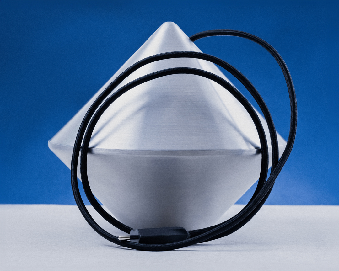 Silver geometric object sits on a white surface against a blue background with a black cable draped around it.