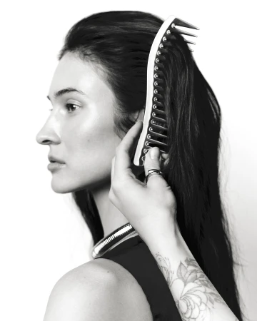 Black and white profile portrait of a woman having her dark hair styled with a large curved comb against a white background.
