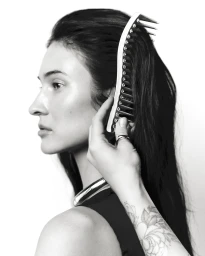 Black and white profile portrait of a woman having her dark hair styled with a large curved comb against a white background.