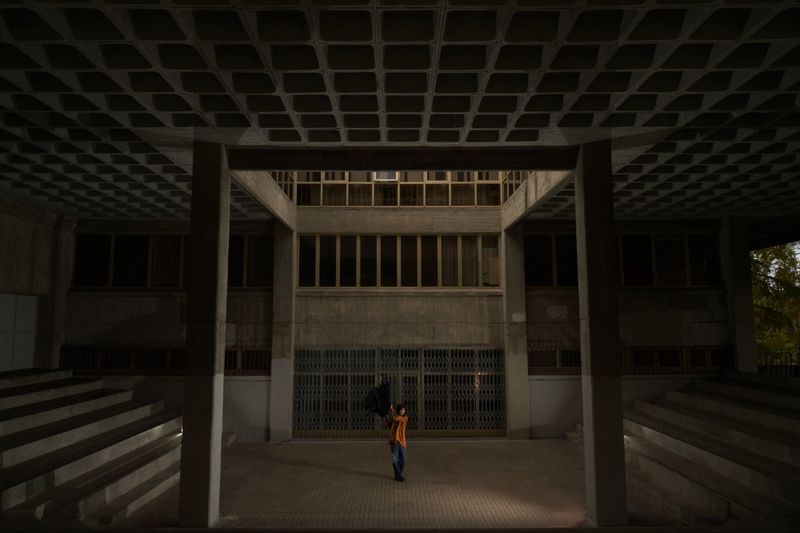 A person walks into a concrete building at night, under a patterned ceiling with square coffers, illuminated by a light source on the ground.