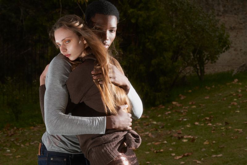 Two models in an embrace against a natural outdoor backdrop, blending fashion and nature in a visually compelling composition.