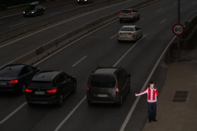 High-angle view of a person hitchhiking by a multi-lane highway at night with moving cars