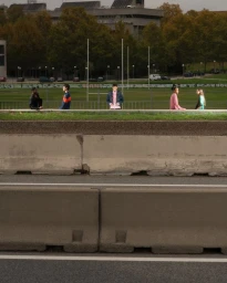 Group of five models standing in a row along a concrete barrier with a sports field and buildings in the background