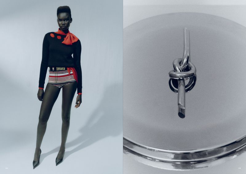 Fashion editorial shot of an African woman in a black sweater, striped shorts and heels posing against a gradient gray background.