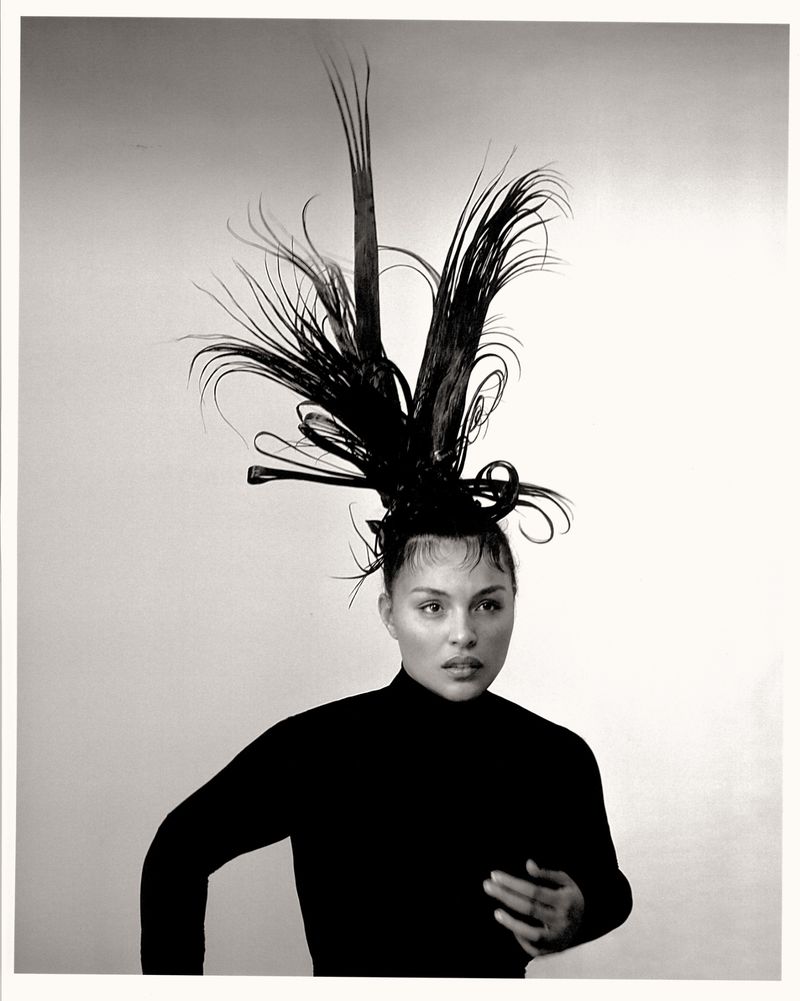 Black and white portrait of an adult female with sleeked hair and an elaborate sculptural hairpiece with feather-like extensions.
