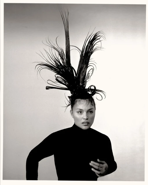 Black and white portrait of an adult female with sleeked hair and an elaborate sculptural hairpiece with feather-like extensions.