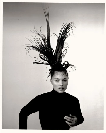 Black and white portrait of an adult female with sleeked hair and an elaborate sculptural hairpiece with feather-like extensions.