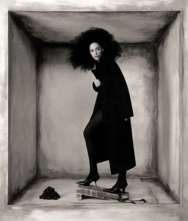 Monochrome fashion shot of a woman in a dark coat and heels stepping on a wooden block inside a painted square, artistic expression.