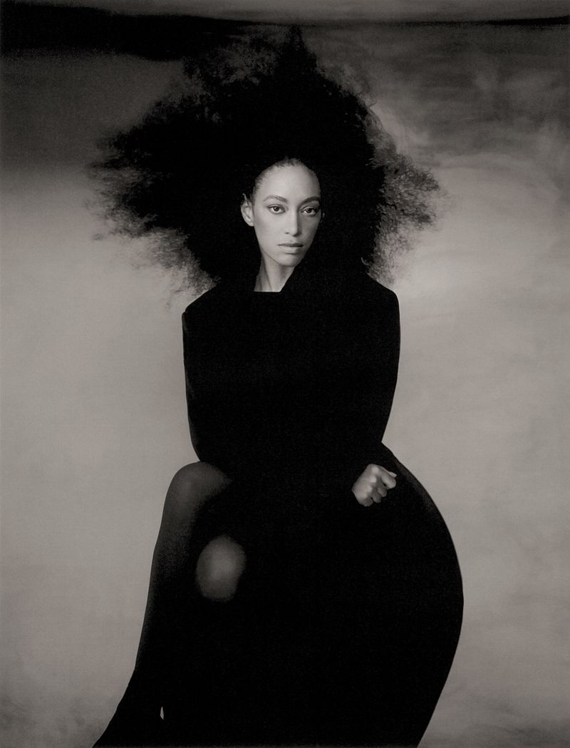 Model Paloma Elsesser with voluminous dark hair wearing black attire against a moody textured studio backdrop