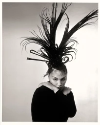 Model Paloma Elsesser with sculptural feathered headdress wearing black top against plain background