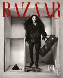 Model Paloma Elsesser in dark leather jacket holding structured handbags inside architectural grey studio space