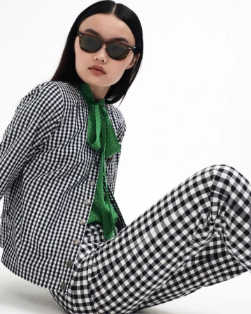 Brunette woman poses in black and white gingham jacket, green polka dot blouse, and matching pants against a bright white backdrop.