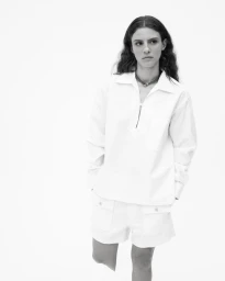 Model wearing a white collared shirt and matching shorts against a plain seamless background.