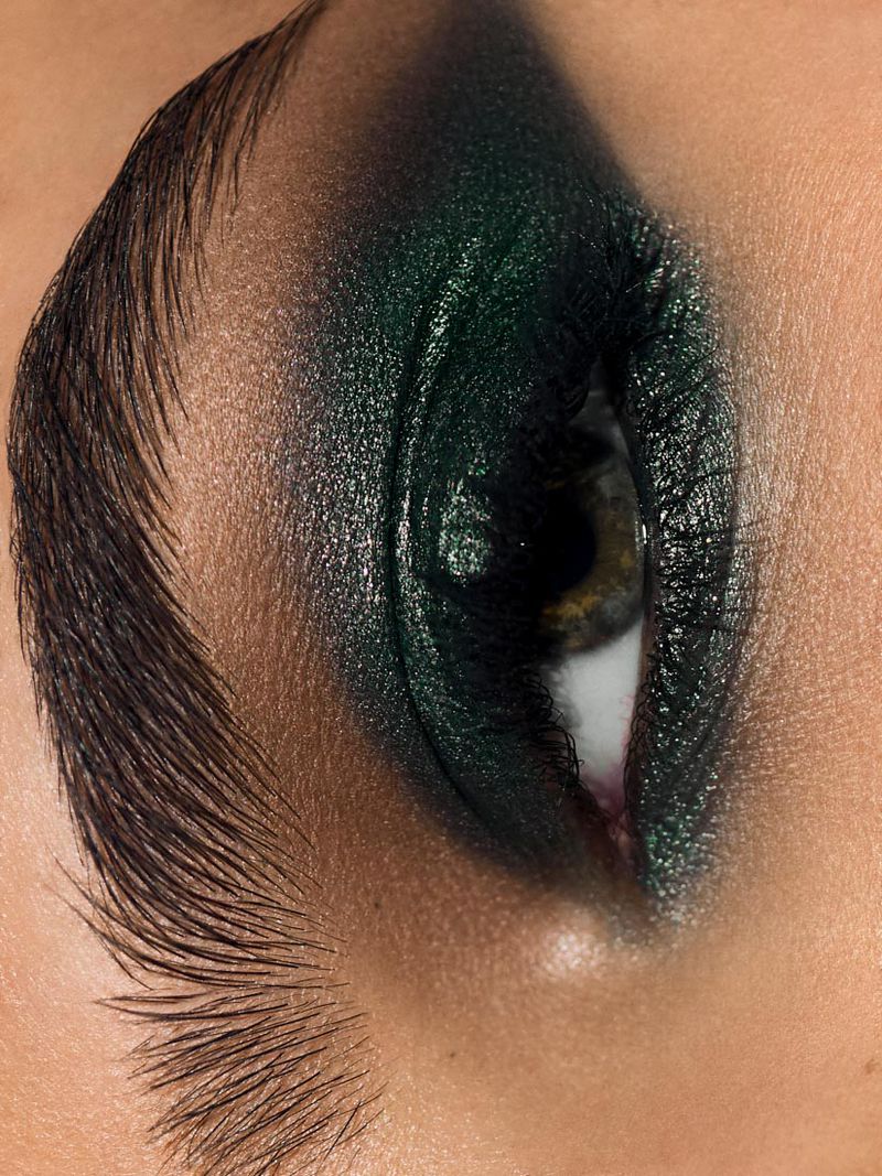 Close-up portrait showcasing an adult female's eye, eyebrow, and skin highlighted with textured, dark green eyeshadow makeup.