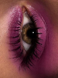 Extreme macro close-up of a human eye featuring vibrant purple eyeshadow and long dark lashes against skin.