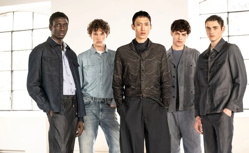 Group of five male fashion models in casual and semi-formal wear, posing indoors against a brightly lit background. Style and presentation.