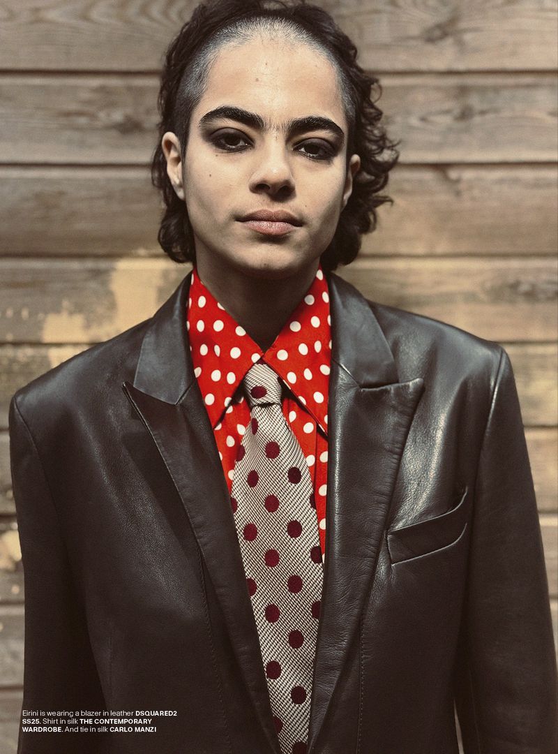 Portrait of a person wearing a red polka dot shirt, tie, and black jacket, posing indoors against a wood paneled wall.