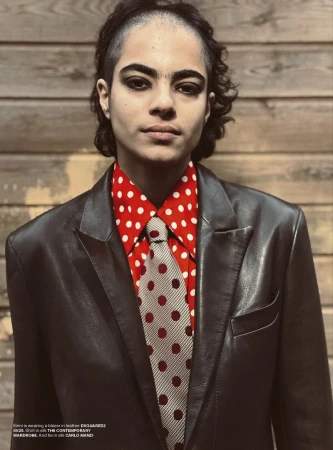 Portrait of a person wearing a red polka dot shirt, tie, and black jacket, posing indoors against a wood paneled wall.