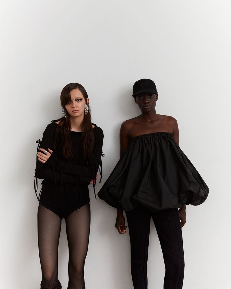 Two fashion models posing in black outfits against a white backdrop, showcasing a modern editorial style in a photo studio.