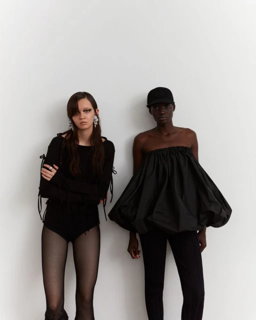 Two fashion models posing in black outfits against a white backdrop, showcasing a modern editorial style in a photo studio.