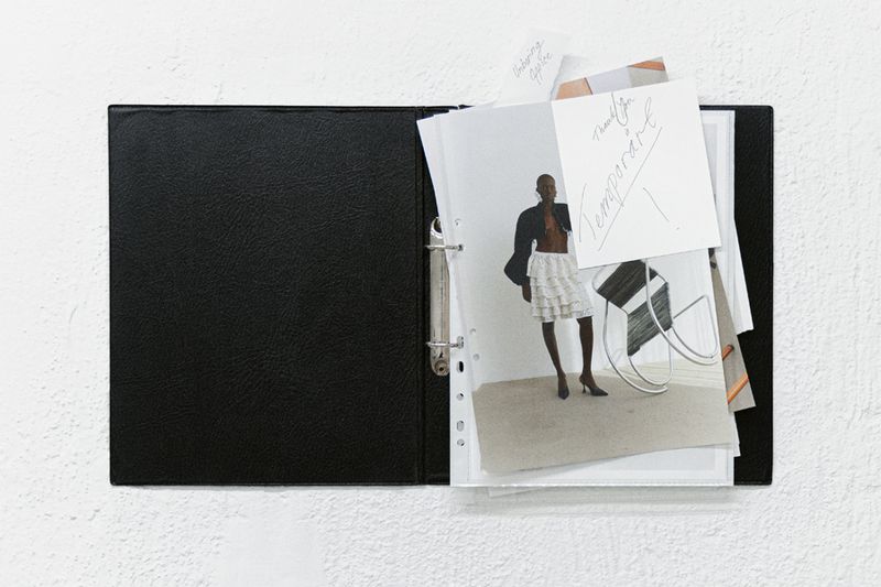 Open black binder displays fashion and interior design photographs against a textured white background, ideal for showcasing creative projects.