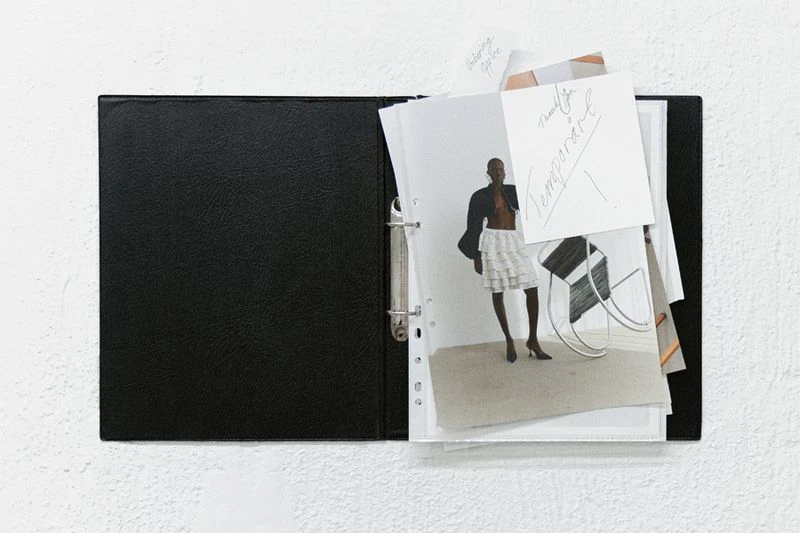 Open black binder displays fashion and interior design photographs against a textured white background, ideal for showcasing creative projects.
