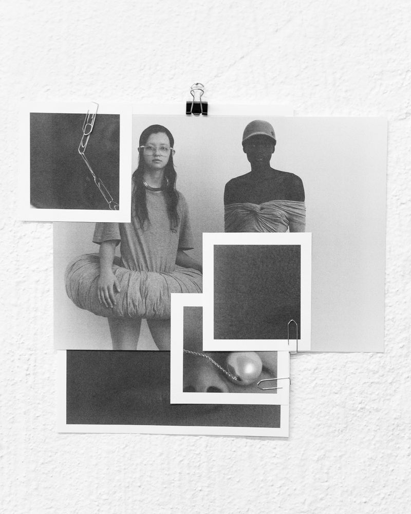 Black-and-white collage of fashion photos pinned to a textured white wall, featuring models, jewelry, and garments.