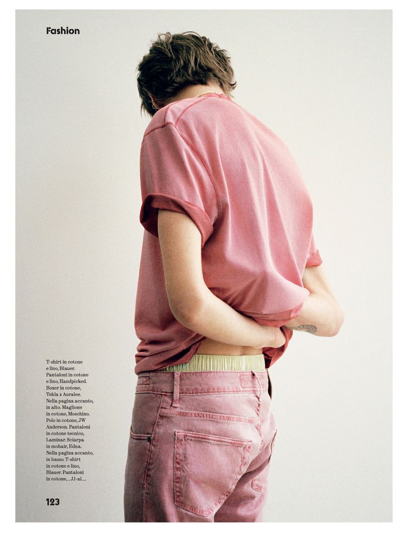 Fashion editorial shot of a person in pink shirt and pants, back turned, showing the waistline in a brightly lit indoor setting.