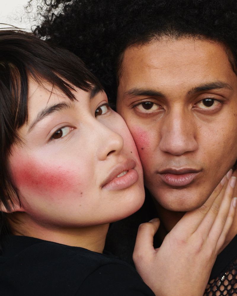 Close-up of an Asian woman and a man with dark curly hair posing together in a photo studio with red blush and neutral lip color.