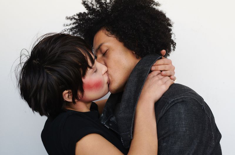 Close-up portrait of an interracial couple in love, embracing and kissing in front of a plain white background, in a modern style.