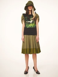 Model wearing an olive green bucket hat, graphic top, and olive skirt against a white background.