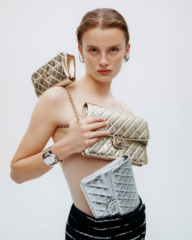 Fashion shot of a woman posing with multiple Chanel quilted handbags in a studio setting, showcasing luxury accessories and elegant style.