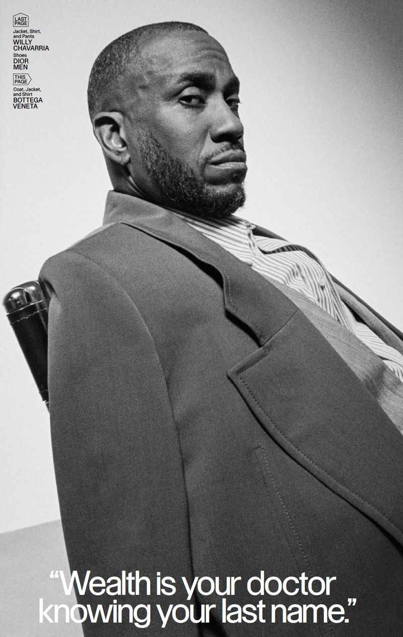 Portrait of a black man wearing a suit, sitting in a chair against a neutral background. Fashion editorial style photography in black and white.