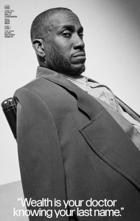 Portrait of a black man wearing a suit, sitting in a chair against a neutral background. Fashion editorial style photography in black and white.