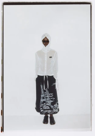Fashion shot of a model wearing a white hooded jacket and black skirt featuring an Eiffel Tower graphic against a bright white backdrop.