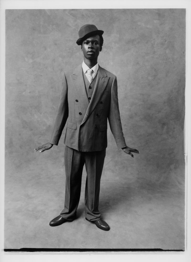 Monochrome portrait of a Black man wearing a suit and bowler hat, looking directly at the camera with neutral facial expression in studio.