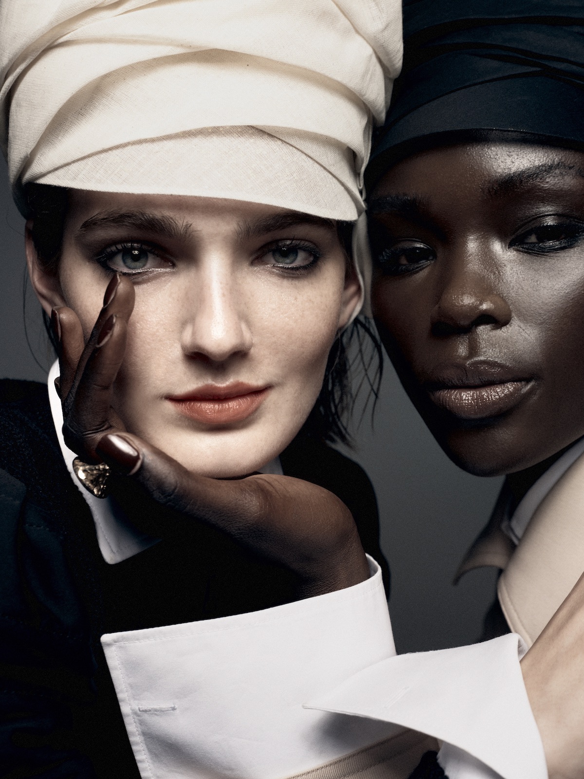 Close-up portrait of two female models wearing head wraps and crisp white collars against a plain neutral background.
