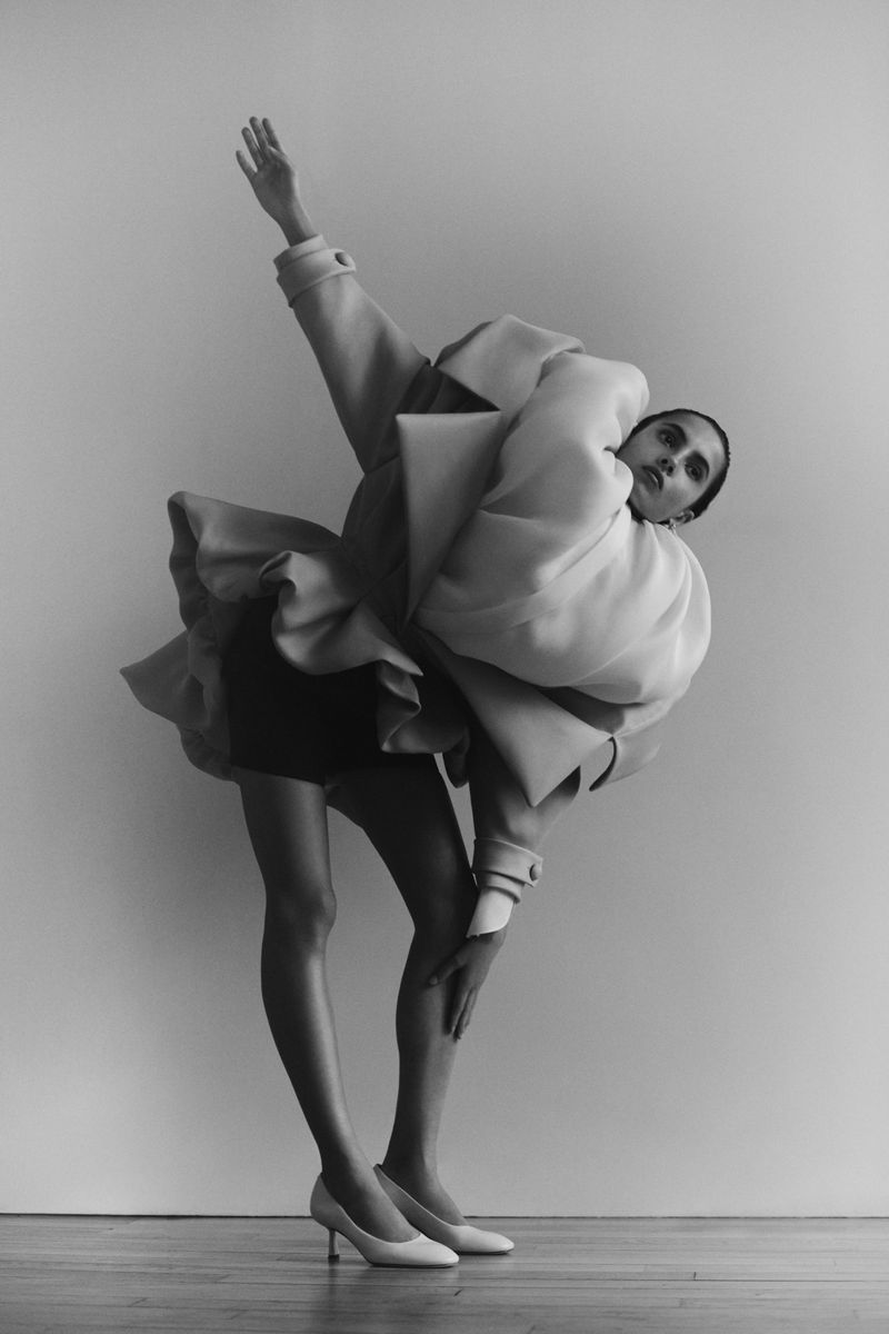 Monochrome fashion shot of a model in an avant-garde coat bending backwards, set against a plain background, highlighting unique design and style.