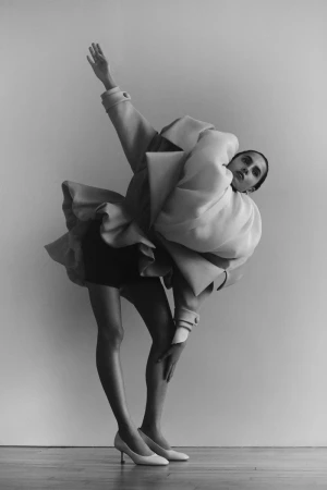 Monochrome fashion shot of a model in an avant-garde coat bending backwards, set against a plain background, highlighting unique design and style.