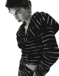 Monochrome fashion portrait of a short-haired woman wearing a textured striped jacket and large circular earrings against white background