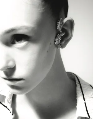 Close-up portrait of a model wearing ornate silver ear cuffs and a white collared shirt against a plain background