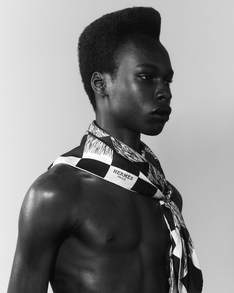 Striking studio portrait of a Black man with afro, adorned with a designer silk scarf; black and white aesthetic, and neutral backdrop.