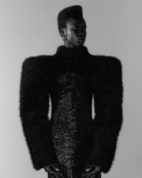 Monochrome portrait of a black man wearing a textured black structured garment against a plain background.