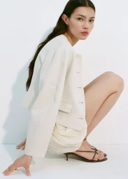 Model Heather Diamond Strongarm crouching against a white studio background wearing a white jacket and skirt.