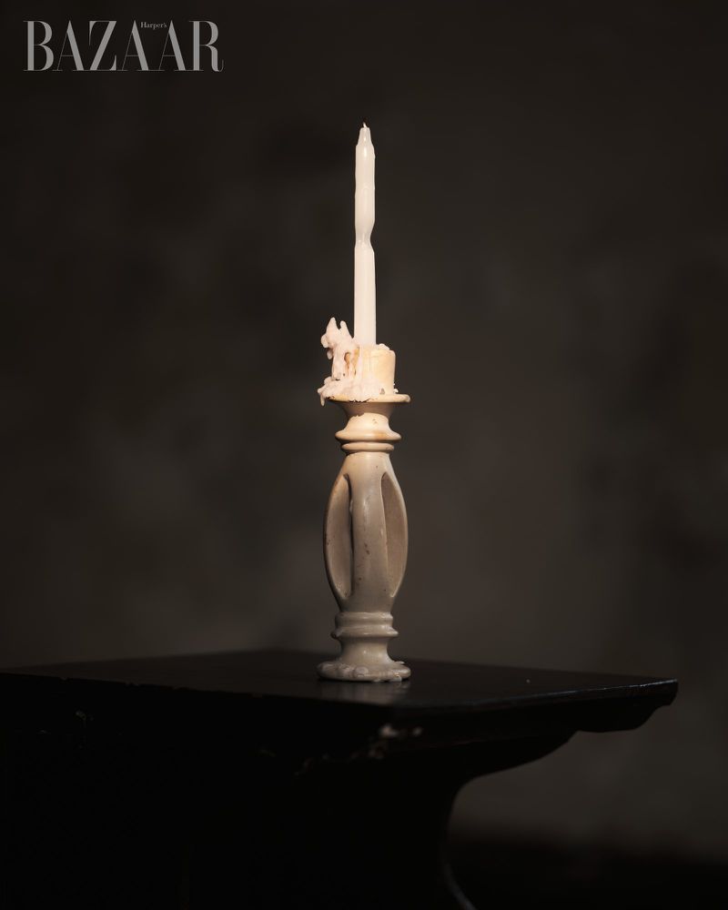 Vintage ivory candleholder with a partially burned white candle on a black table, presented against a blurred dark background.